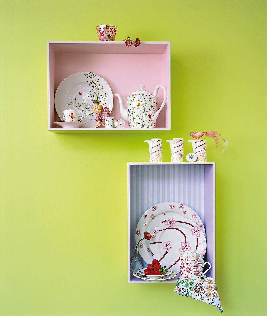 Shelf with porcelain crockery against green painted wall