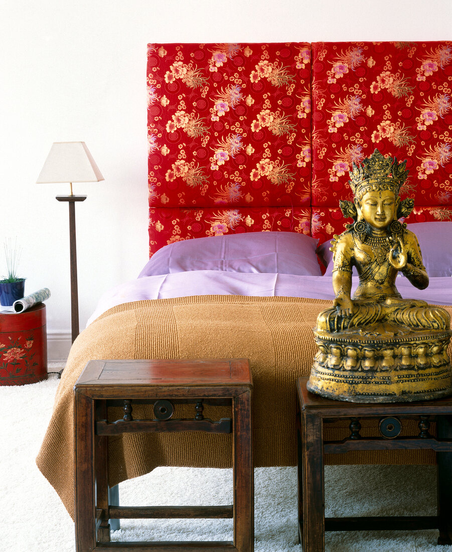 Bedroom decorated in Asian style with red cushions and Buddha statue