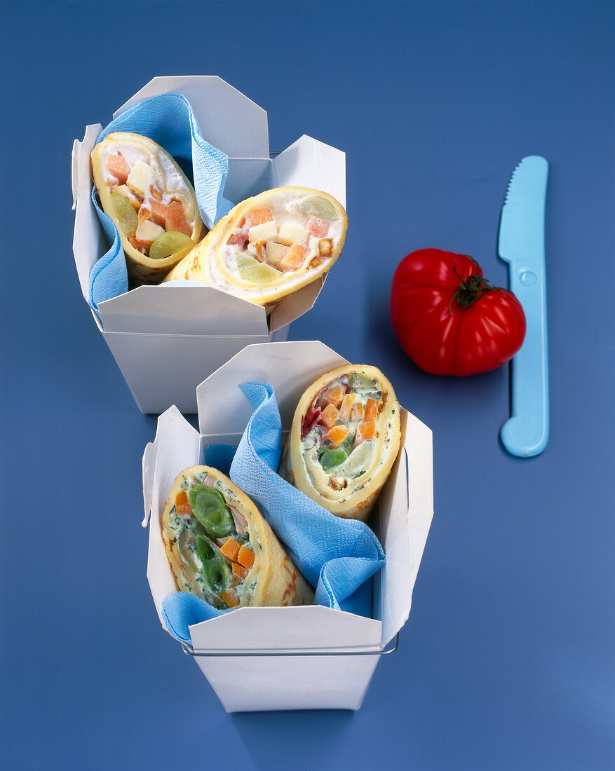 Mini rolls with vegetable stuffing in cardboard box on blue background