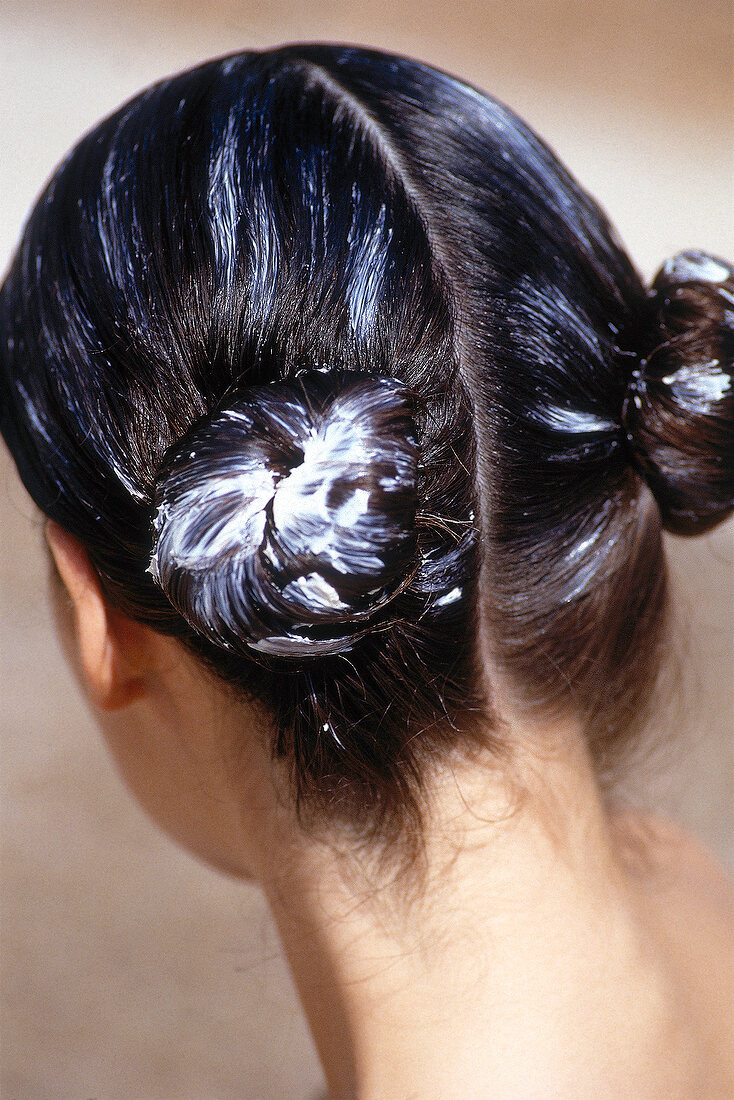 Woman's wet hair middle parted and tied in nodes with cream applied for hair treatment