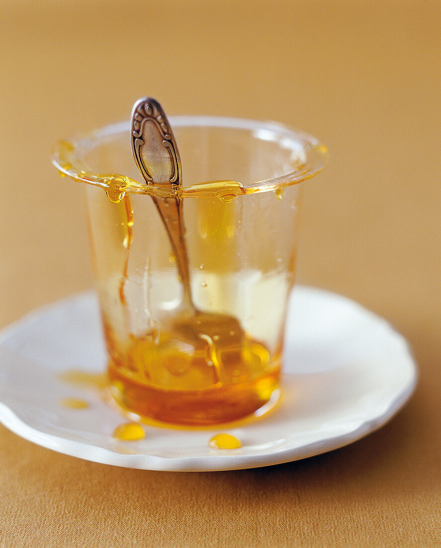 Honey jar with smeared edge and spoon, honey drops on plate