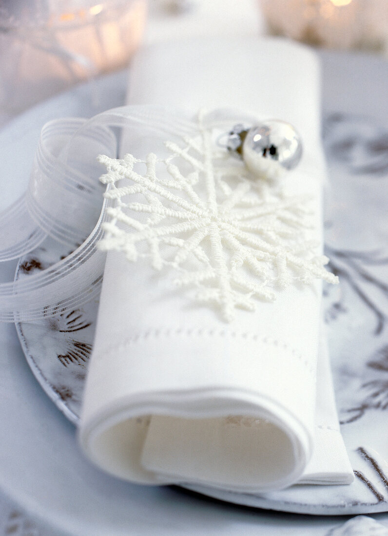 Close-up of white napkin with snow flake and ribbons on plate