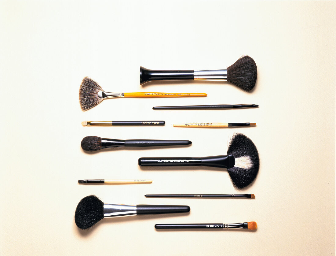Close-up of make-up brushes of different sizes and widths arranged on white table