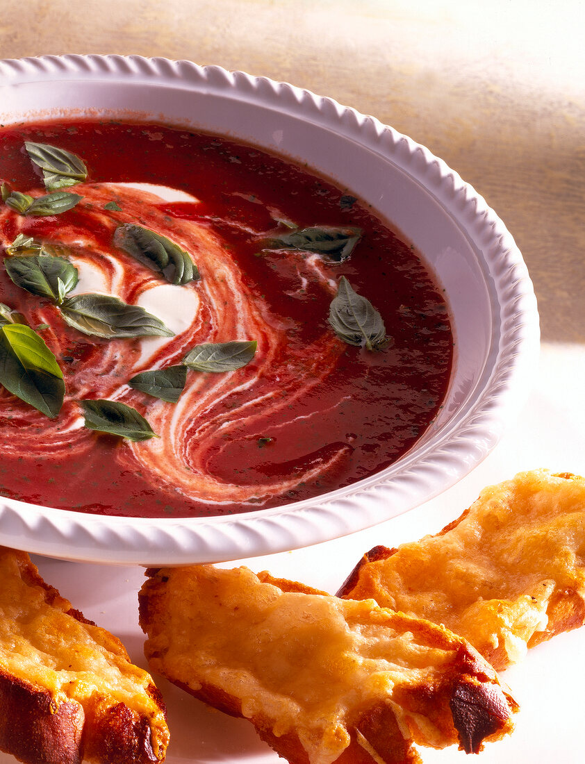 Tomato soup with cheese in bowl beside croutons