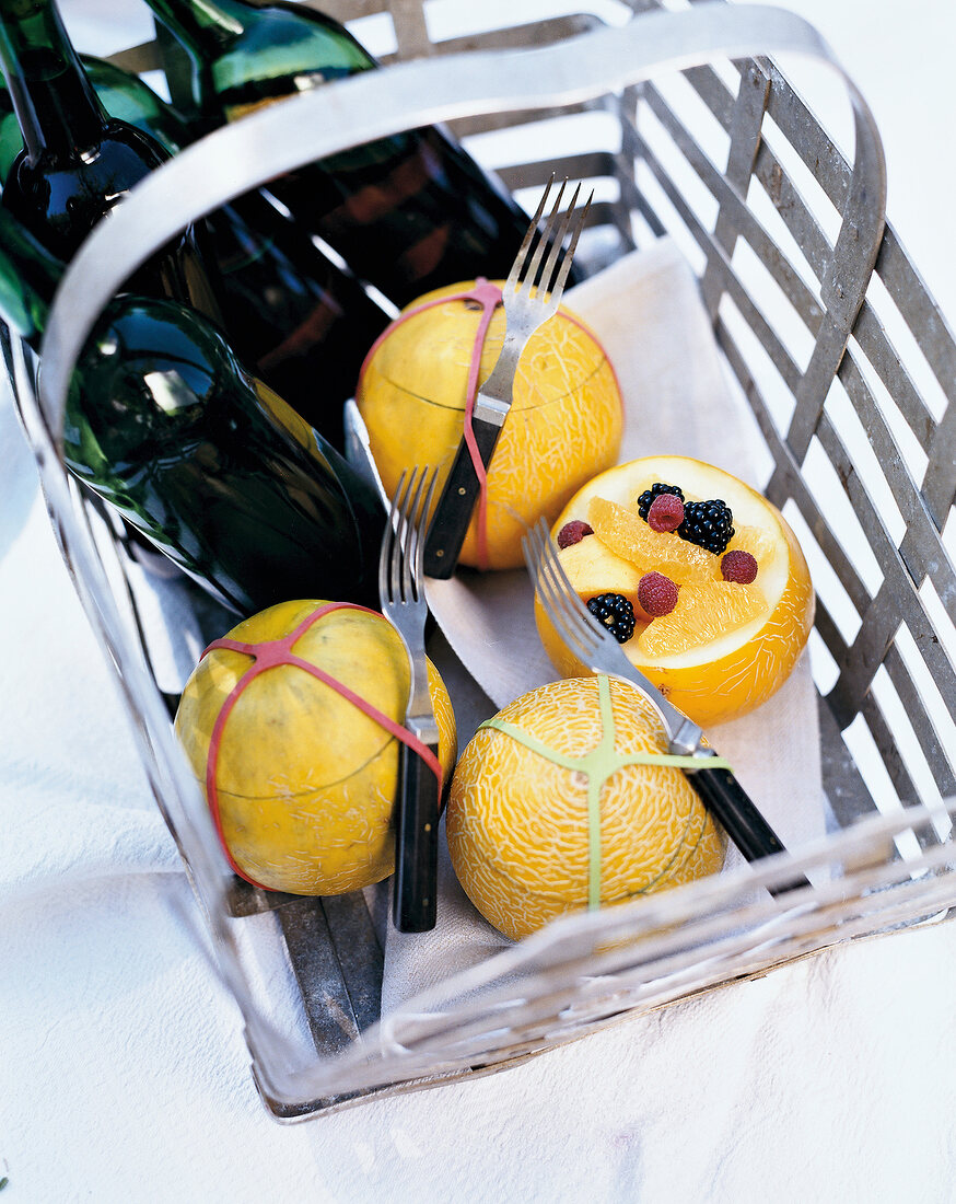 Fruit salad in galia melon with fork and wine bottles in basket