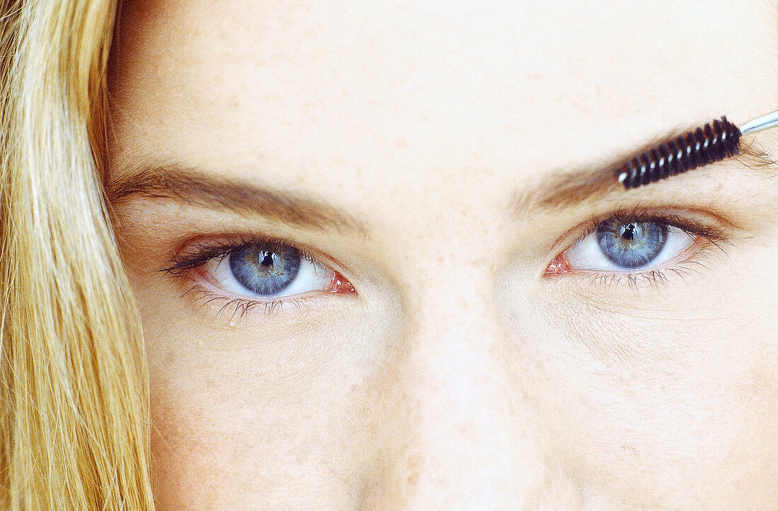 Close-up of blue eyed woman brushing her eyebrow with mascara