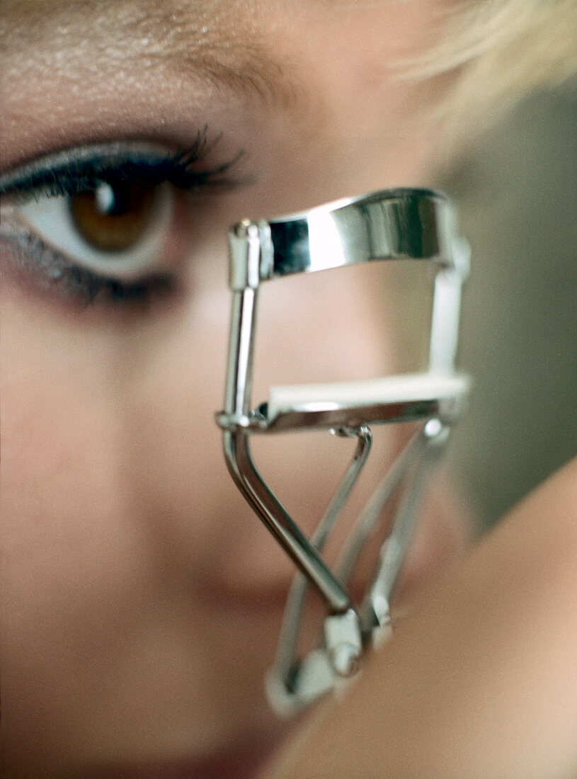 Close-up of woman curling her eye lashes with eye lash curler