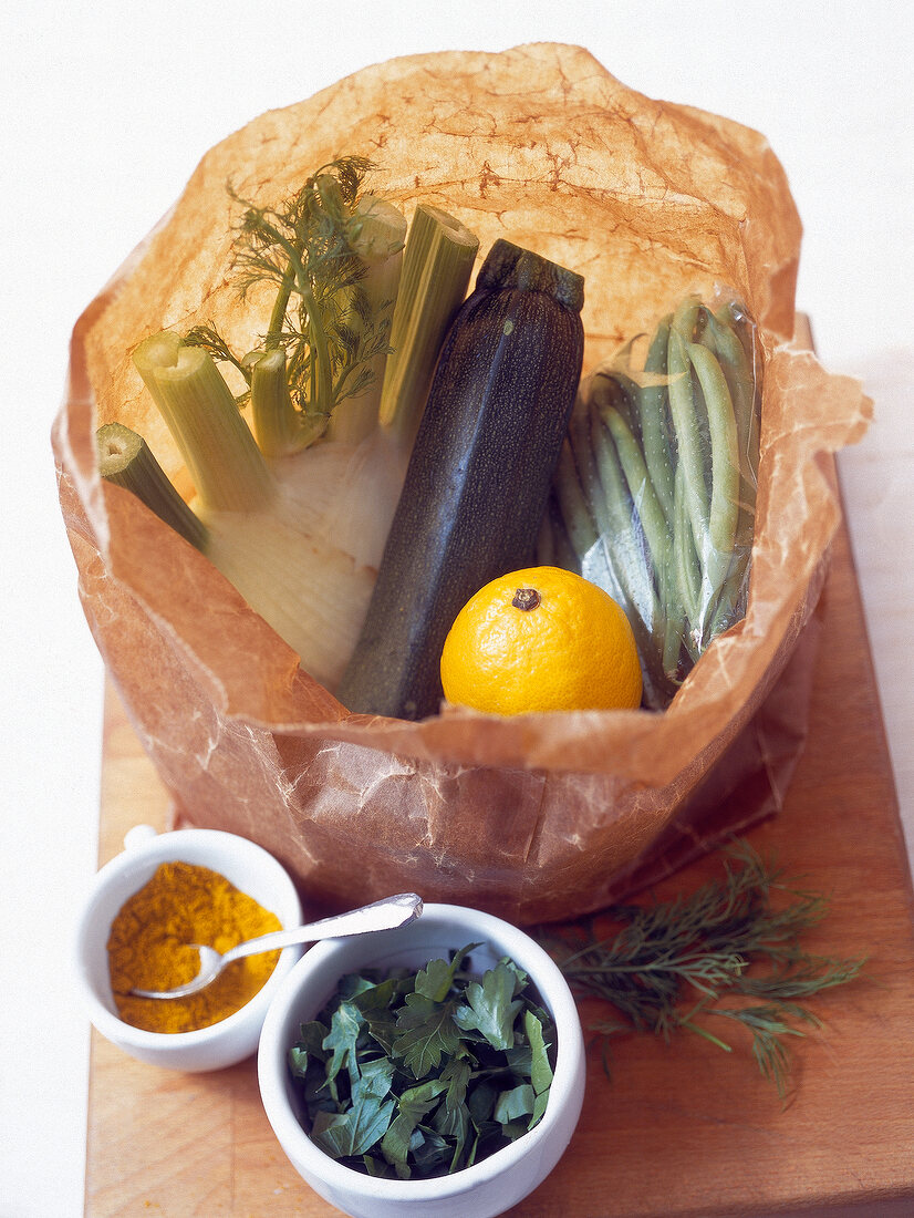 Bag with fennel, beans, zucchini and lemon, turmeric and leaves in bowl on wood