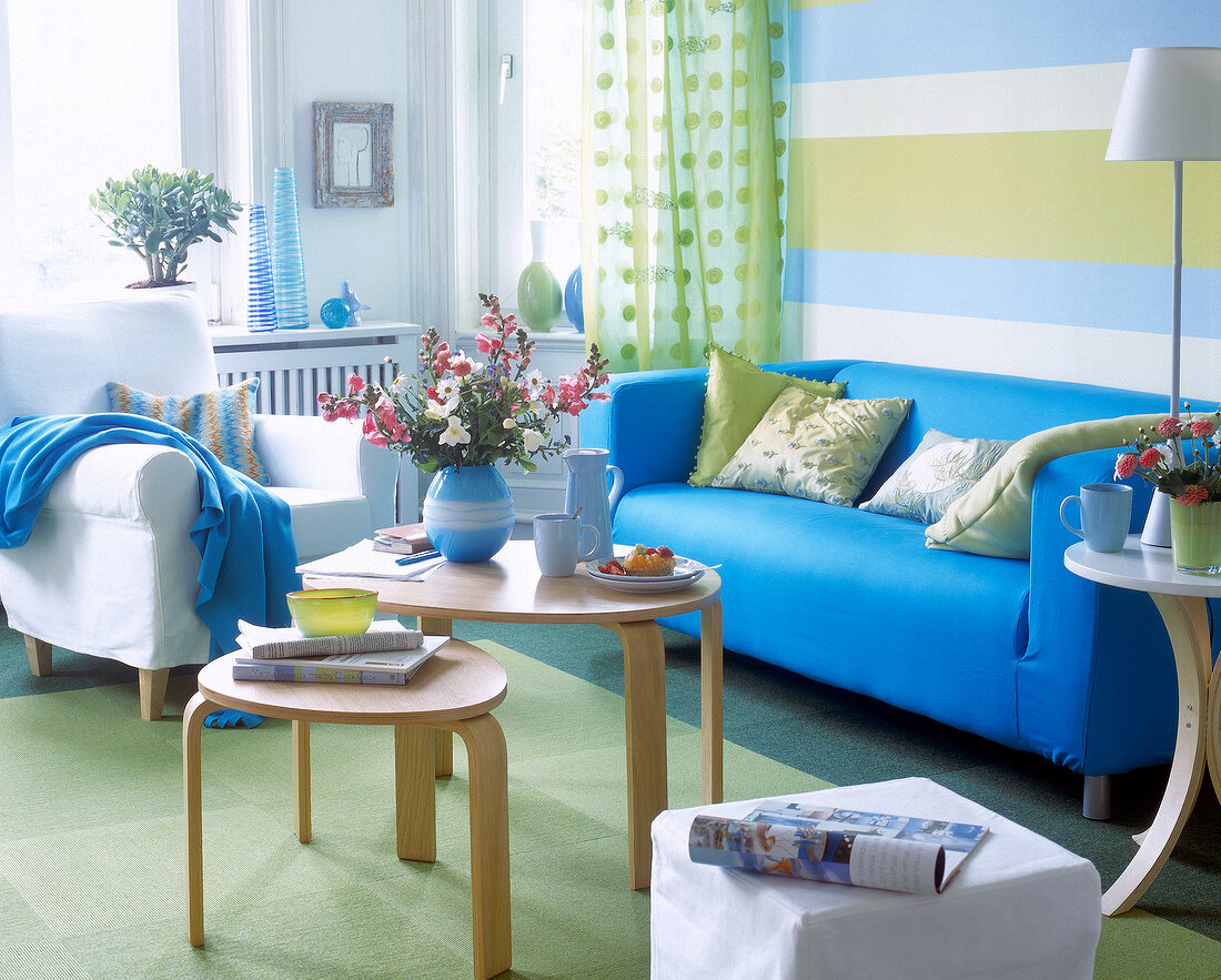 Wohnzimmer mit blauem Sofa und grünen Teppichbodenfliesen, Tische