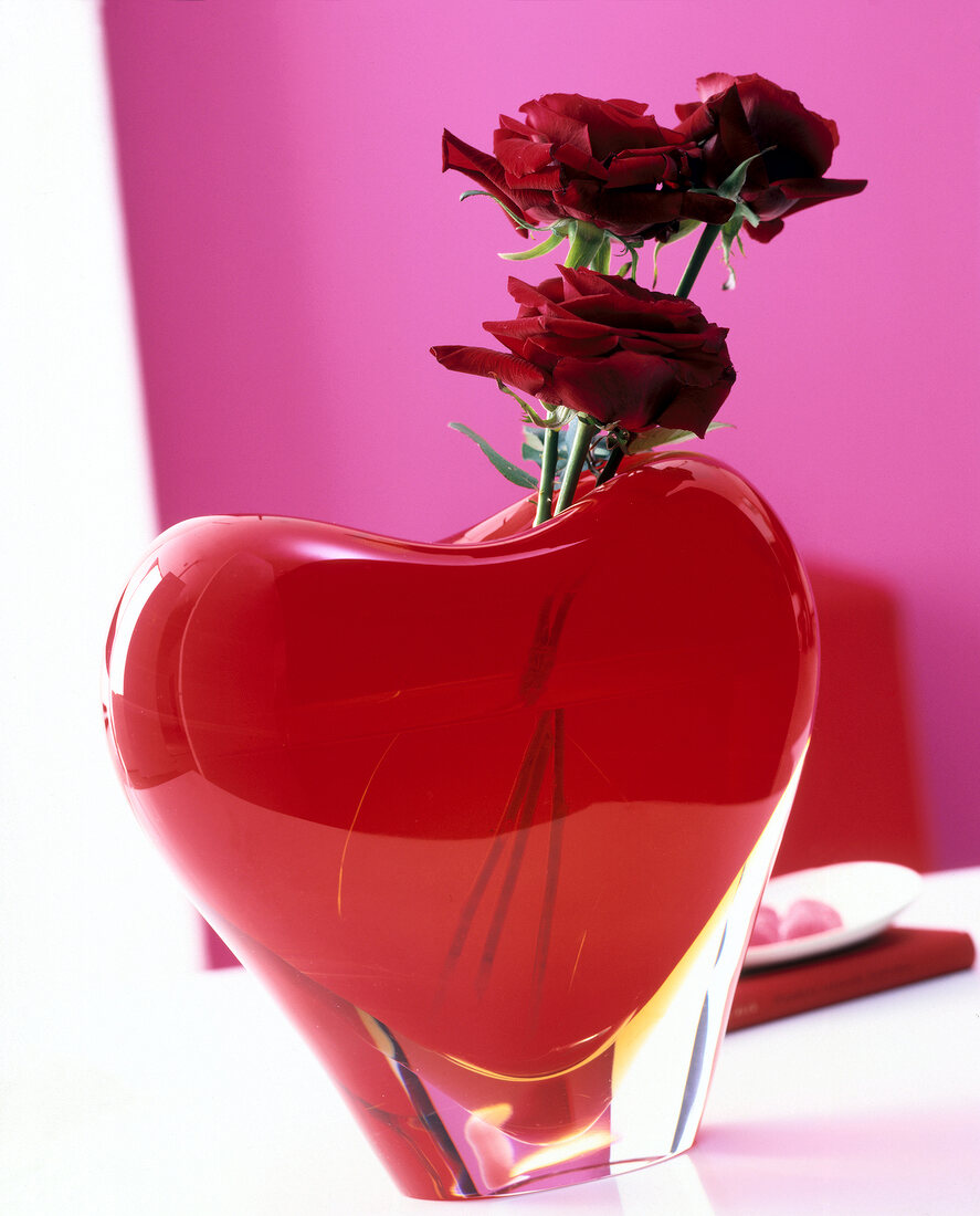Red heart vase with roses on table