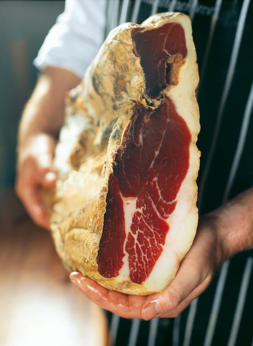 Pork butcher holding a country ham, Rugen, Germany, close-up