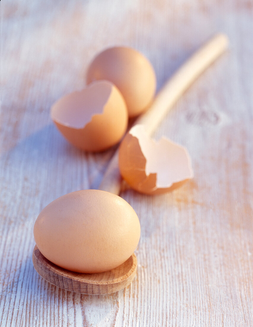 Brown egg on wooden spoon beside brown egg shell