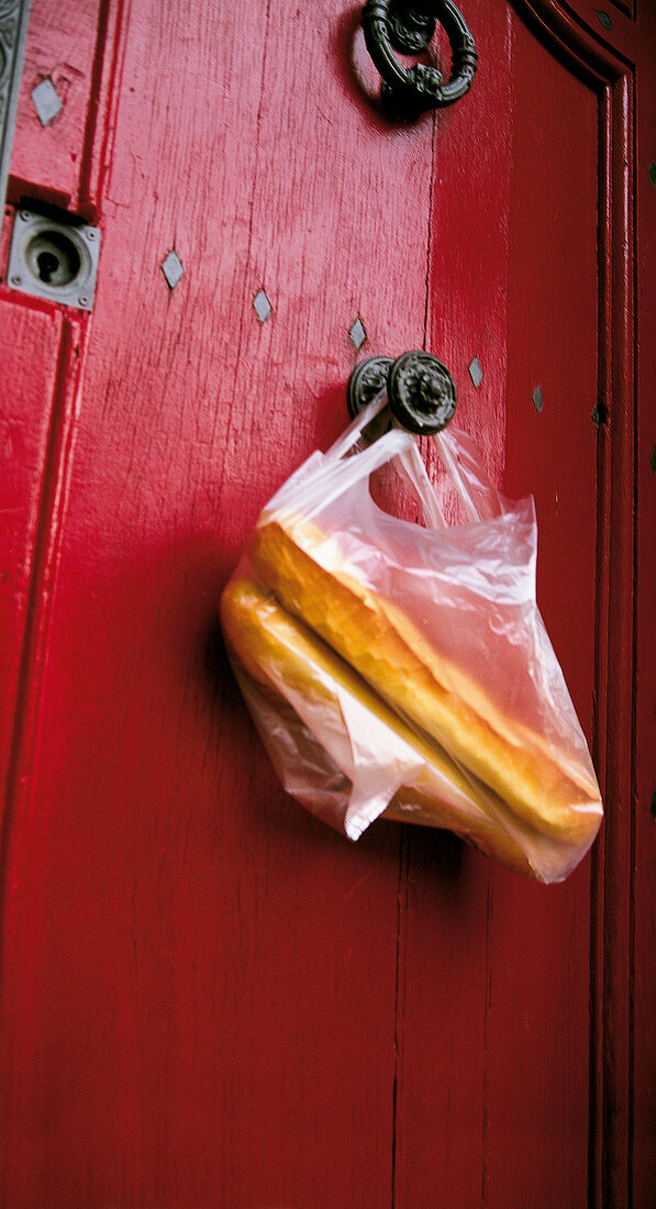 Plastic bag with fresh baguettes hanging on the knob of red door