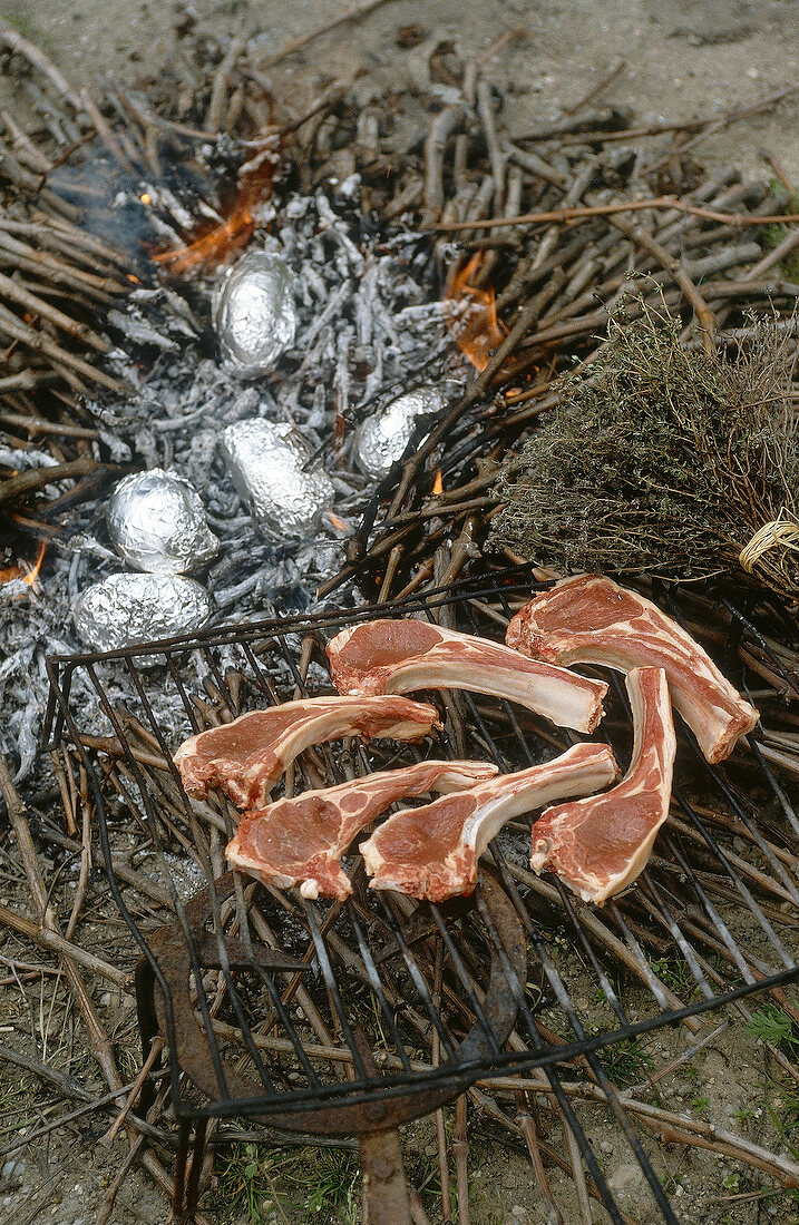 Preparation of lamb chops on the grill and potatoes in aluminium foil