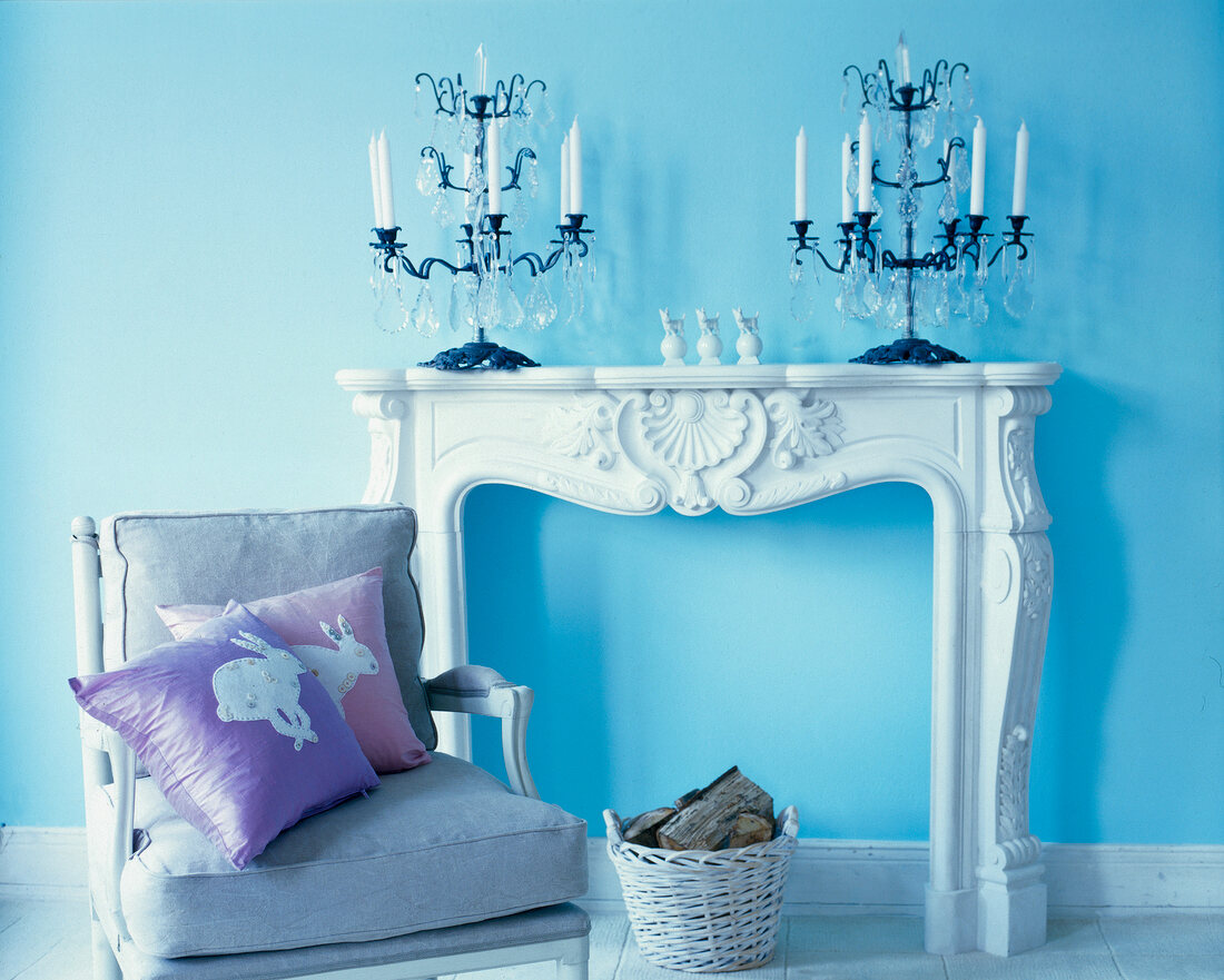 Chair in front of white mantelpiece with iron candlesticks