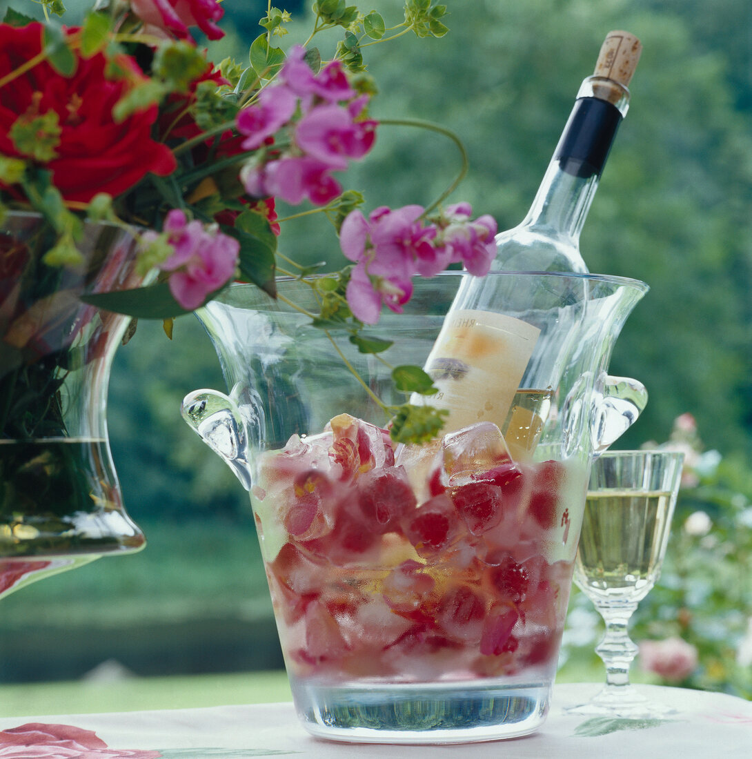 Ice cubes with frozen blossom scroll in wine cooler with flower vase on table