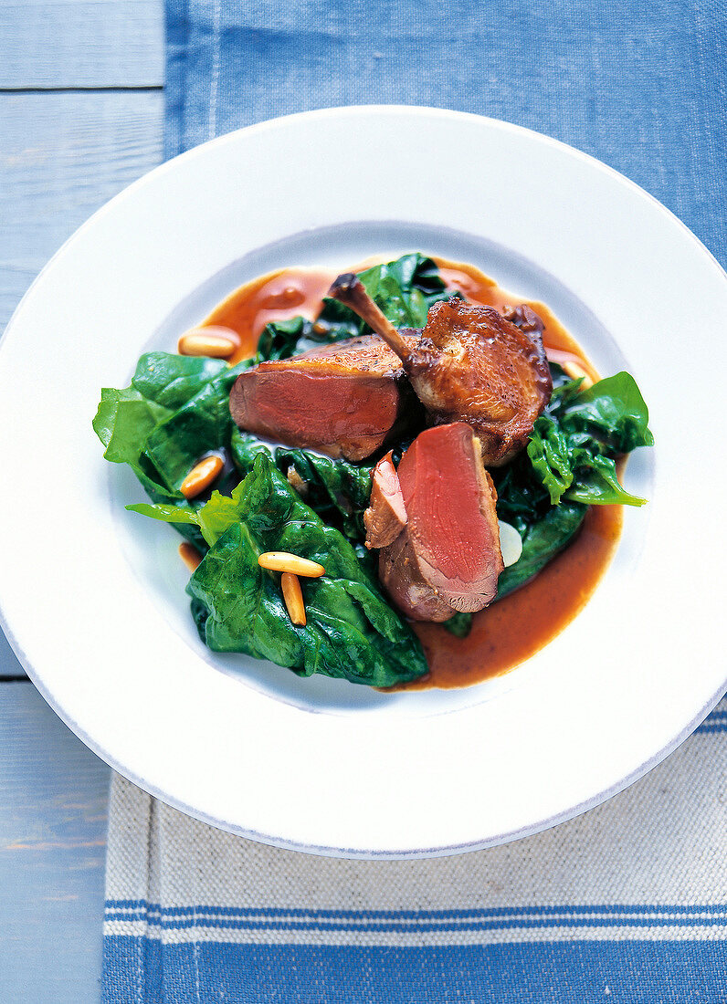 Close-up of pigeon with spinach and pine nuts on white plate