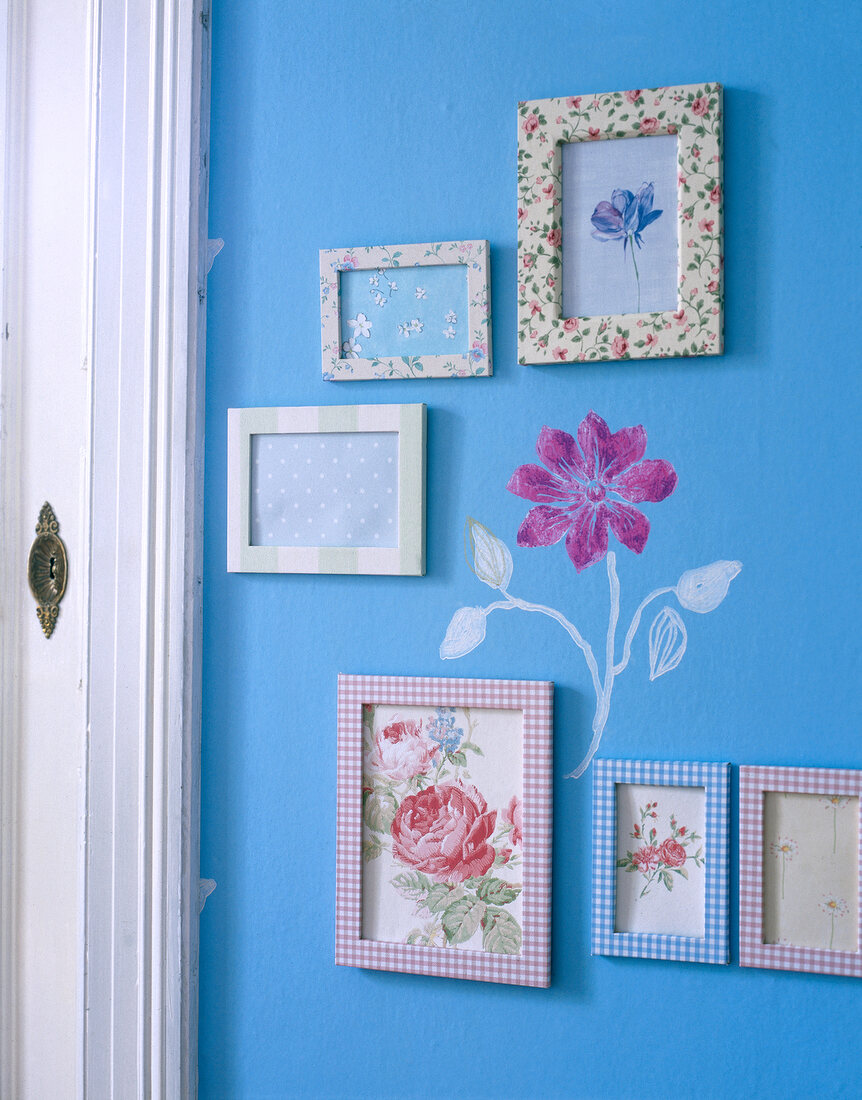 Bunte Bilderrahmen hängen an blauer Wand mit aufgemalter Blume