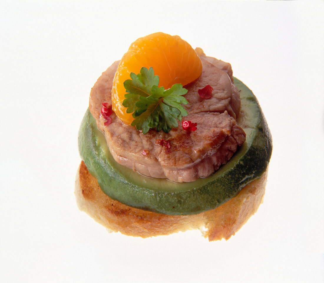 Close-up of baguette with veal medallions, avocado and mandarin on white background