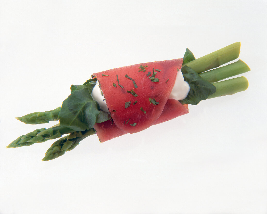 Close-up of asparagus roll with smoked ham, sour cream and horseradish on white background