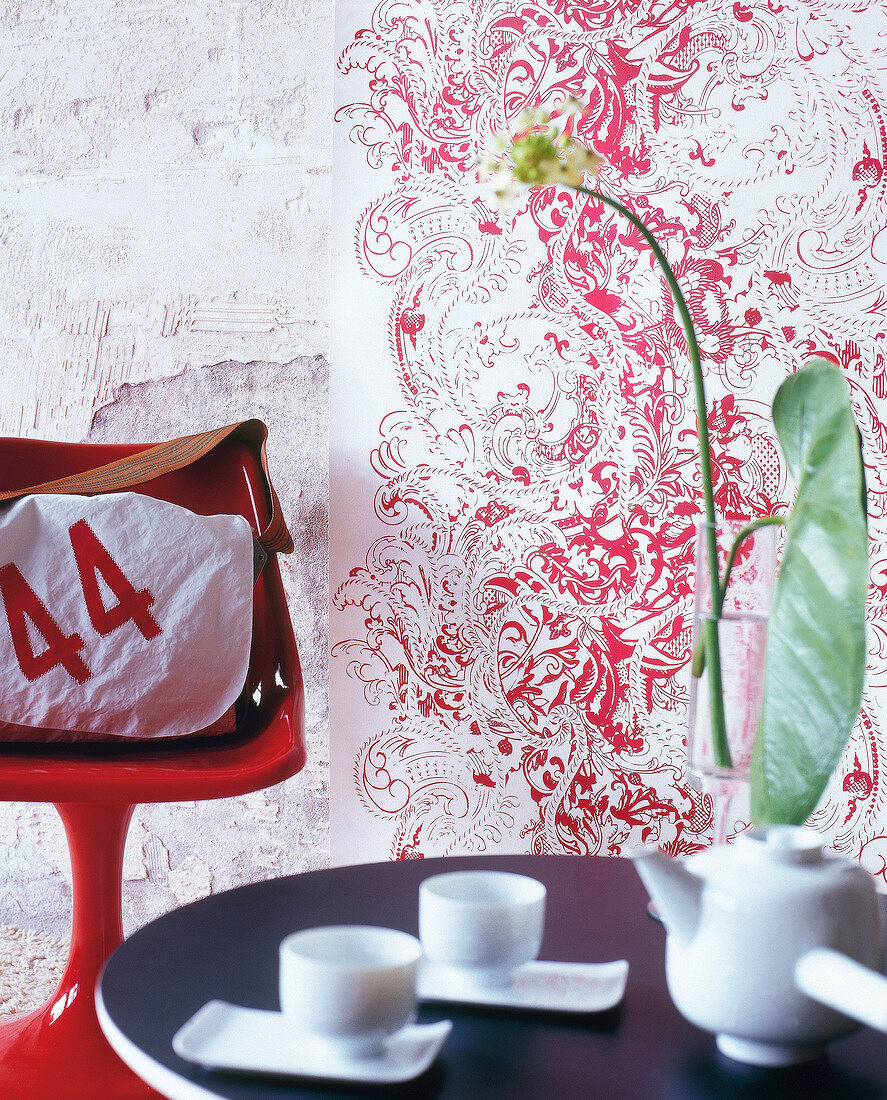Wallpaper strip with opulent pattern beside red chair and white bag