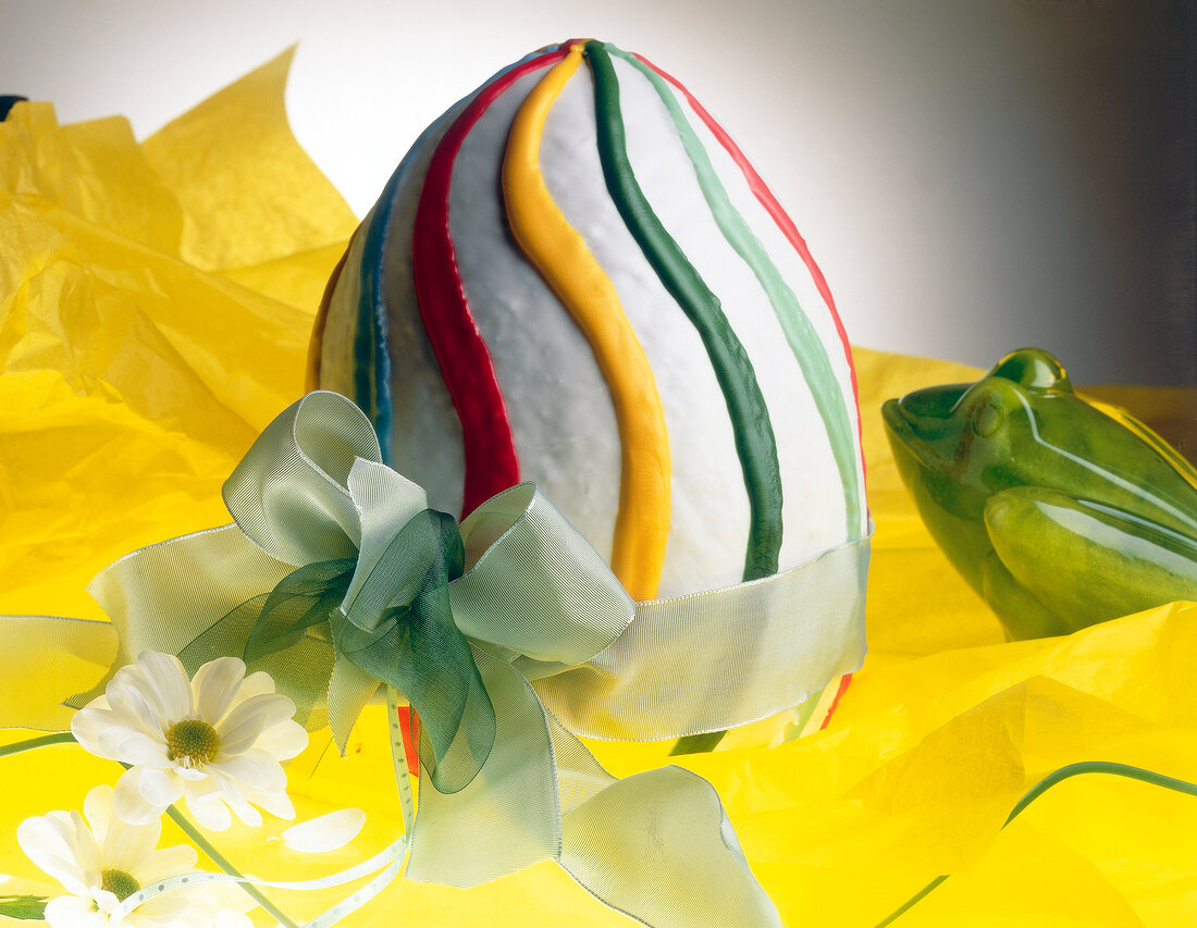 Close-up of colorfully painted Easter egg filled with eggnog cream and white ribbon