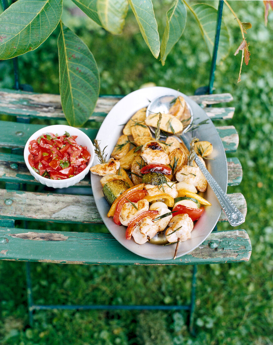 Baked potatoes and gefluegelspiessen on plate with spoon on wooden bench