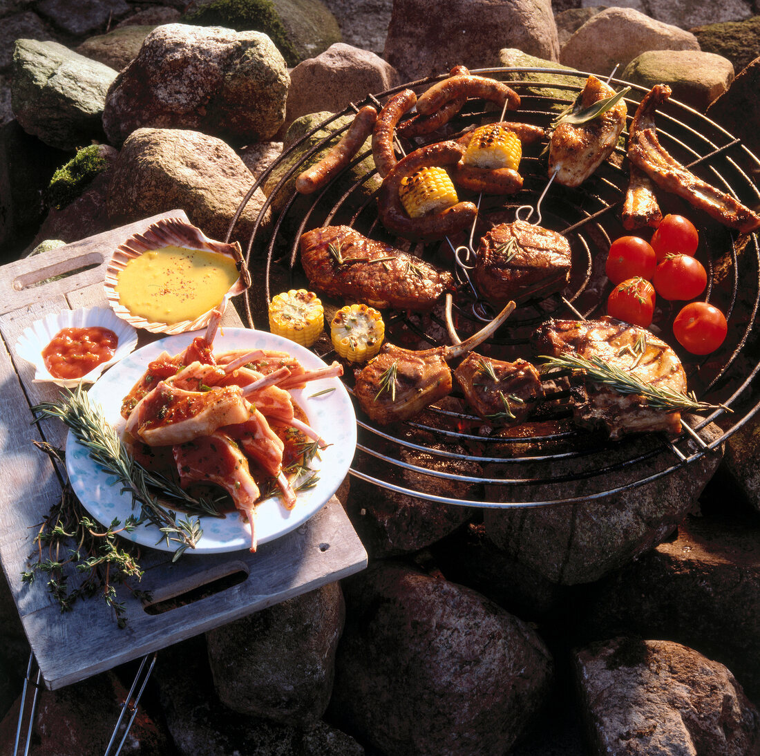 Sausages, tomatoes, corn, dips, rosemary and several kinds of meat served on a rock table