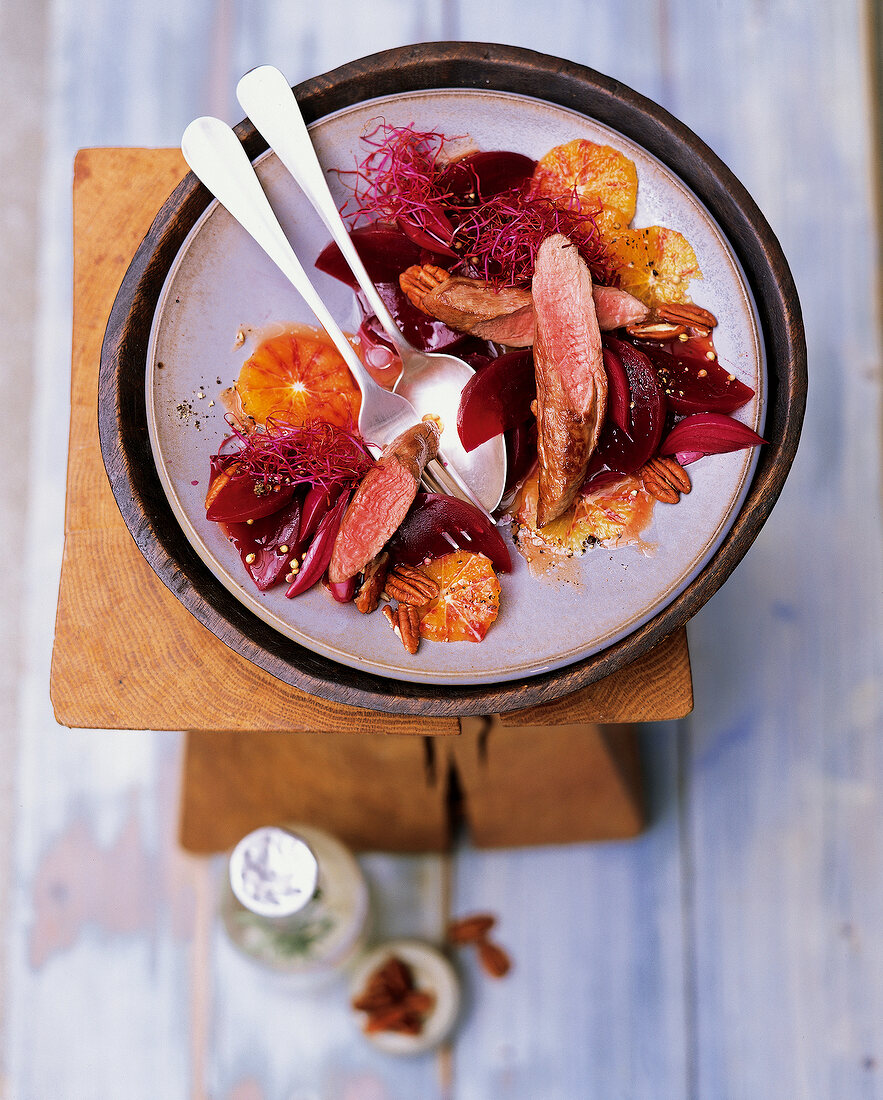 Salad with lamb fillet, beetroot, orange and pecans on wooden table