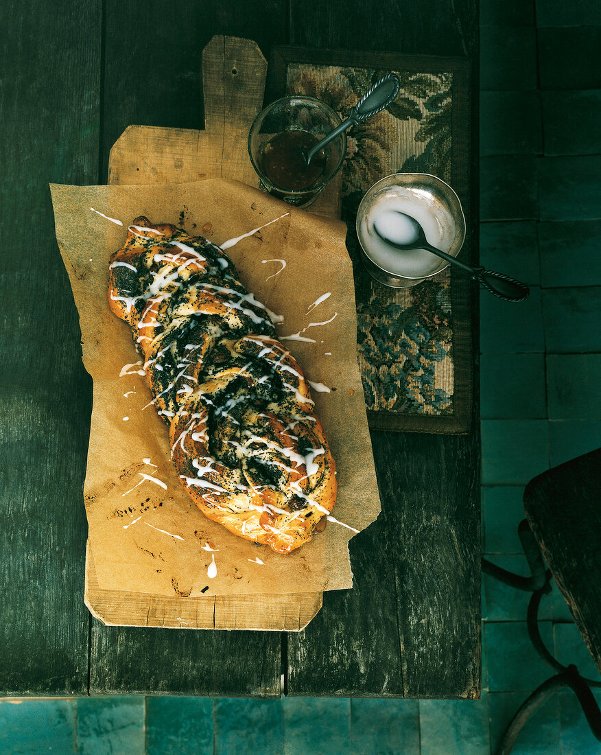 Poppy seed plait on paper and two cups with frosting on wooden table