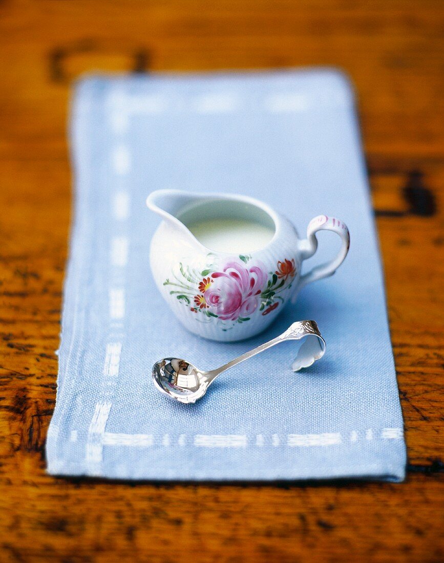 A small cream jug on a light blue napkin with a silver spoon