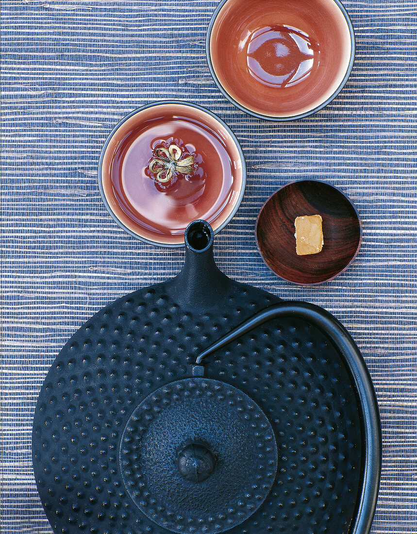 Cast iron teapot beside clay bowls and candied ginger