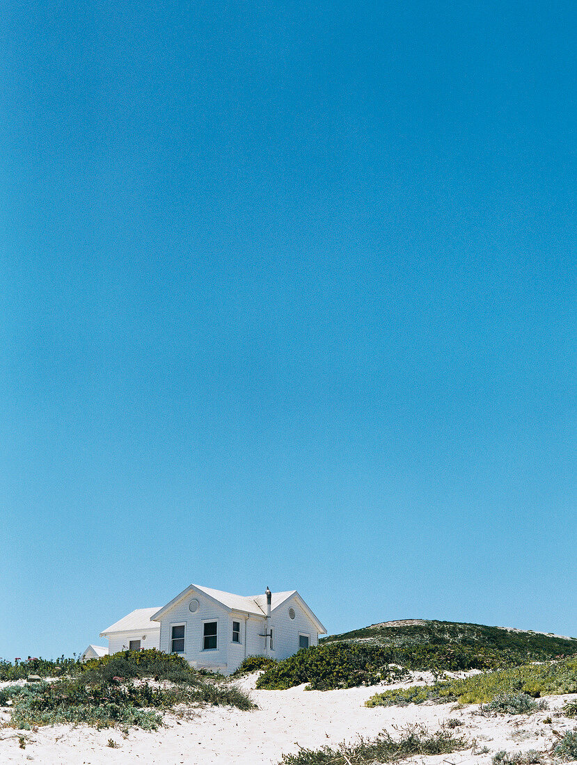 White wooden house surrounded by sand dunes on beach