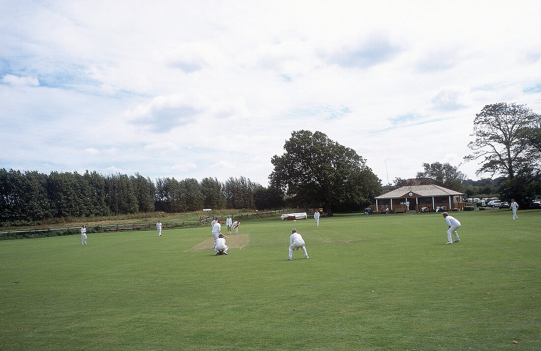 Crickers in winter sportswear playing cricket on green ground, England, UK