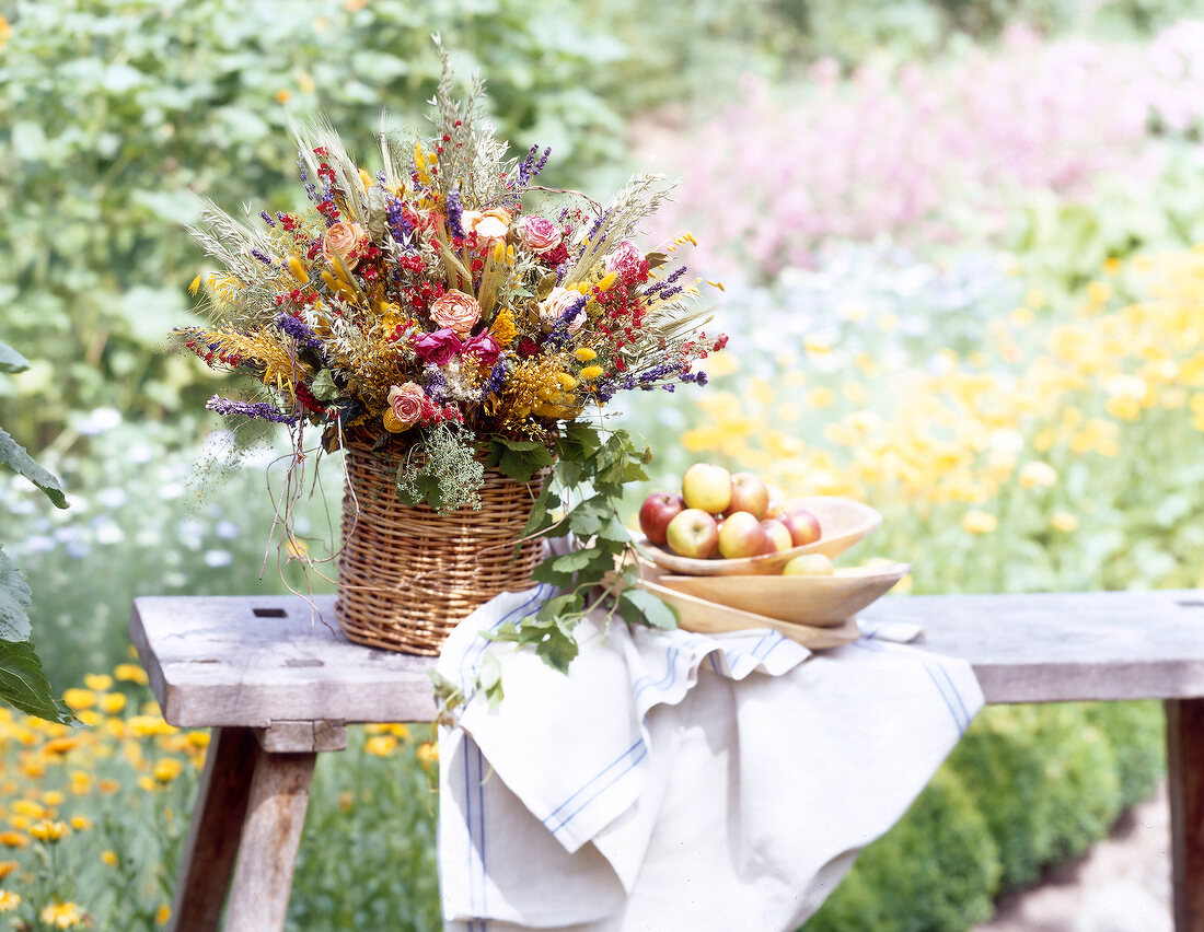 Colourful summer bouquet in wicker basket with napkin and bowl of fruits on side