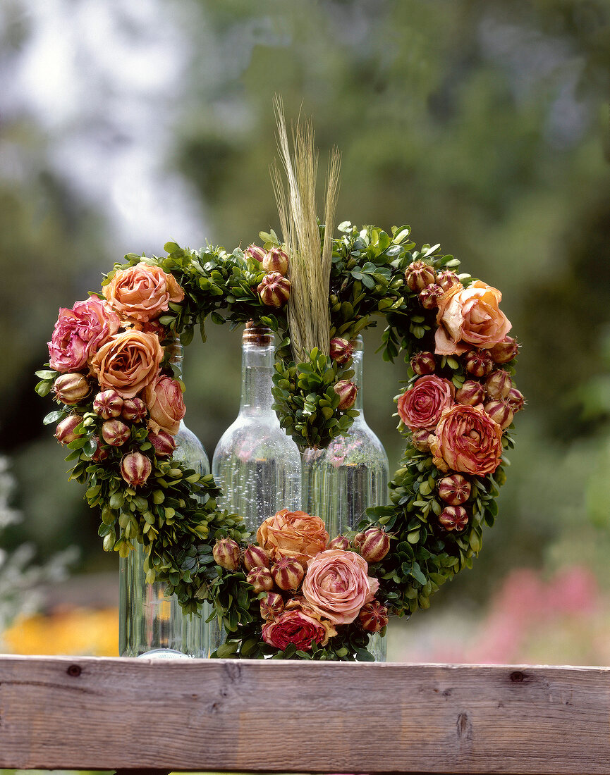 Heart shape wreath with pink roses and boxwood on glass bottles