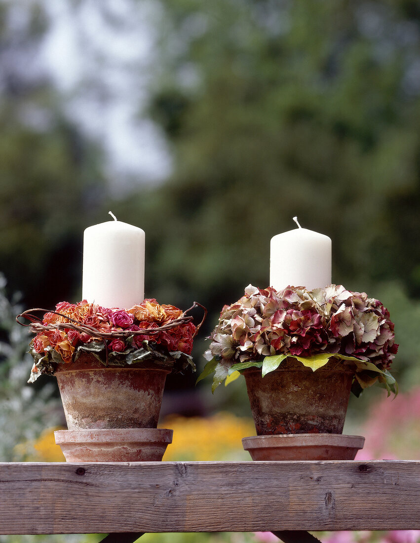 White candles in flower pots with dry rose flowers and hydrangeas on wood