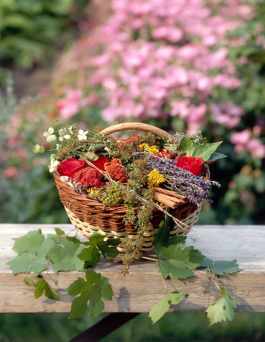 Wicker basket with scented bouquets of herbs, berries and flowers on wood