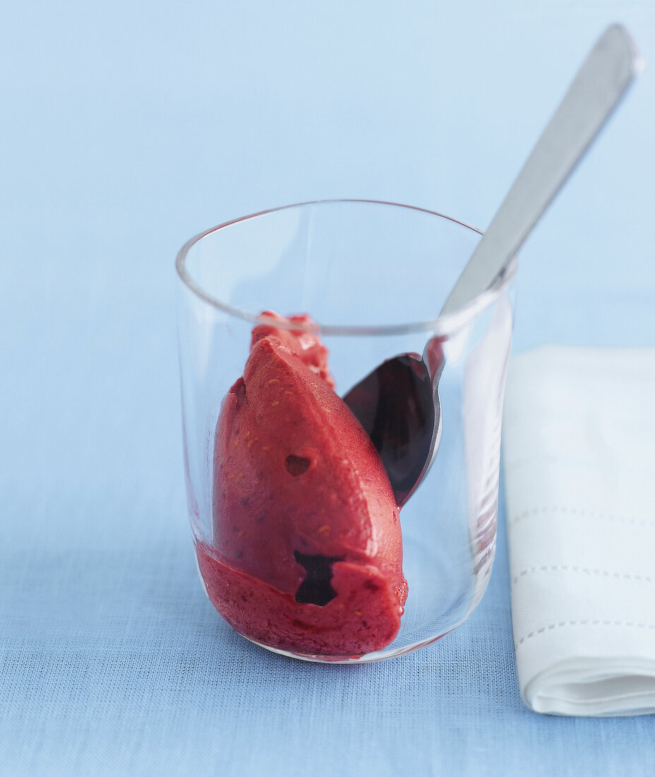 Raspberry in a glass with spoon against blue background