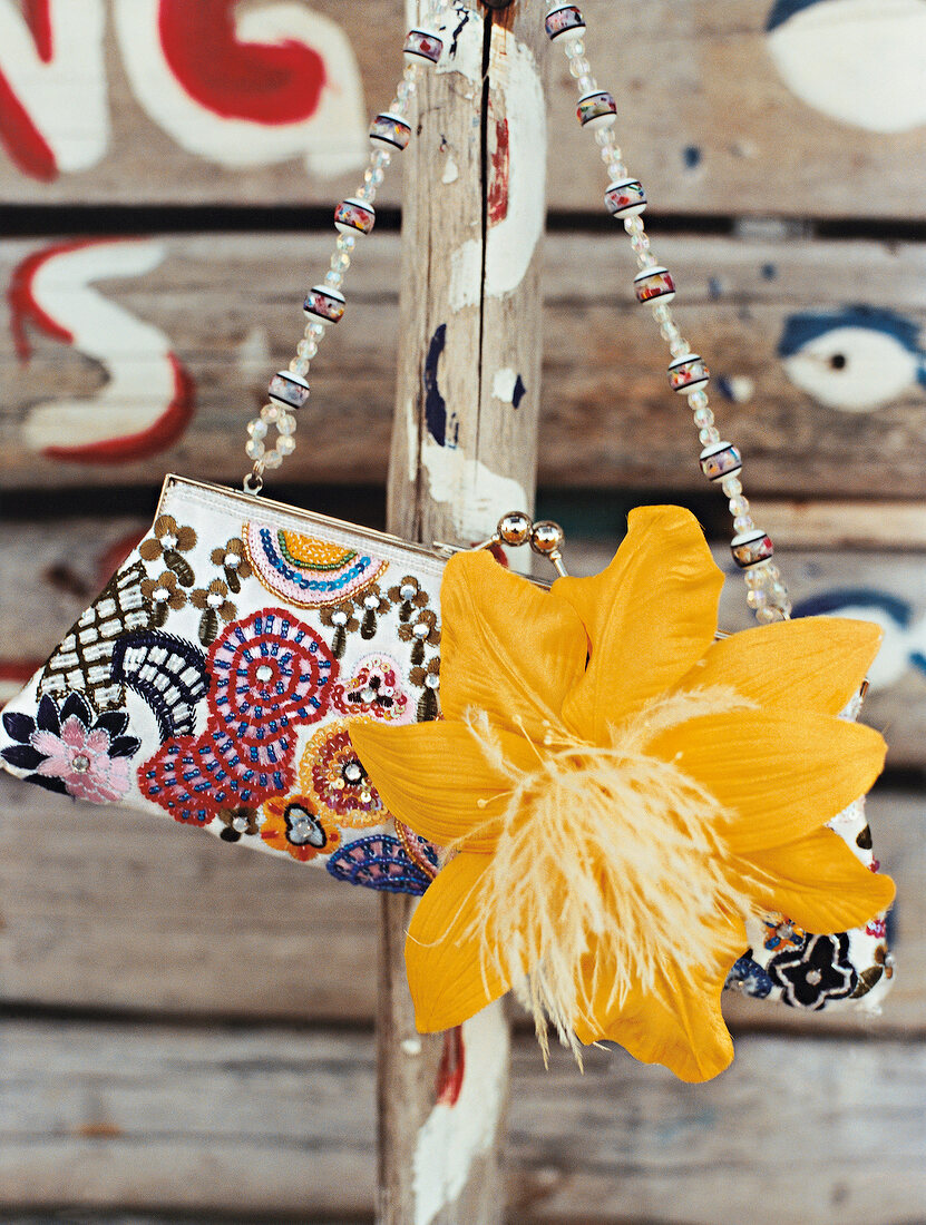 Close-up of playful embroidered purse with yellow flower hanging on bamboo