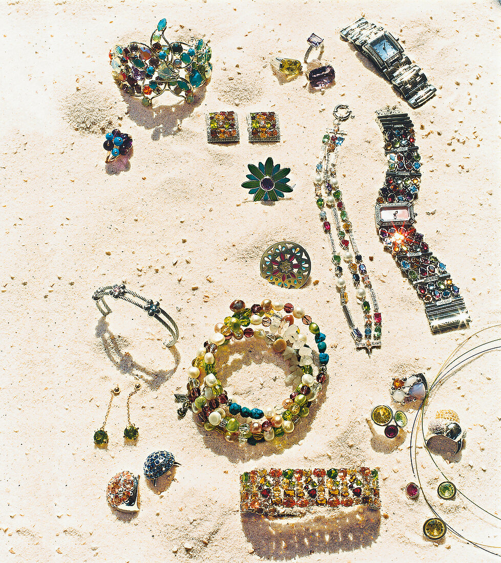 Various watches and jewellery scattered on white sand