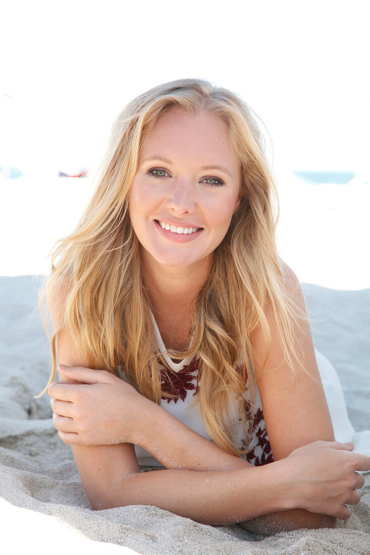 Blonde woman in a bright dress on the beach, smiling at the camera