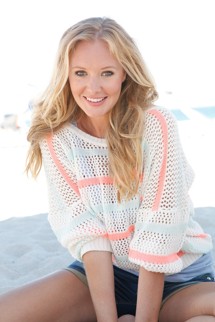 Blonde woman in a white sweater on the beach, smiling at camera