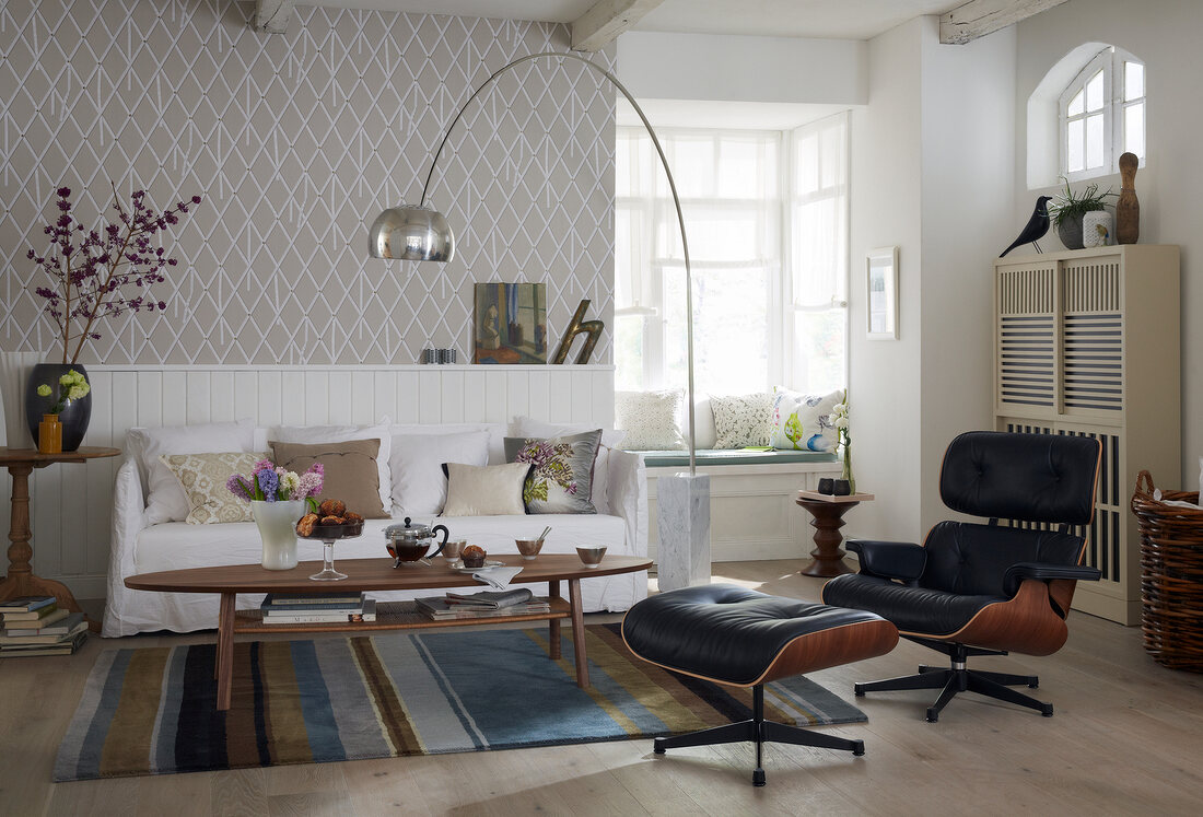 A living room in a mixture of styles with a sofa, an arc lamp, a leather armchair with a foot stool and a sitting area in the bay window