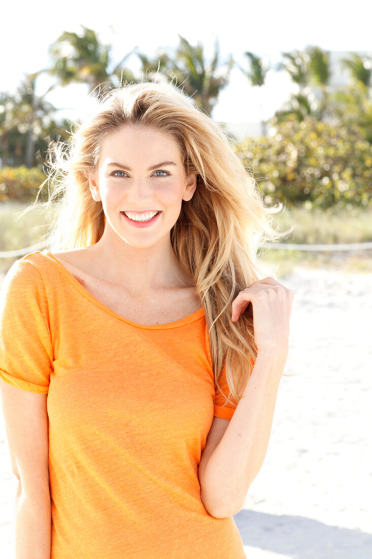 Blonde Frau mit langen Haaren in orangefarbenem T-Shirt am Strand