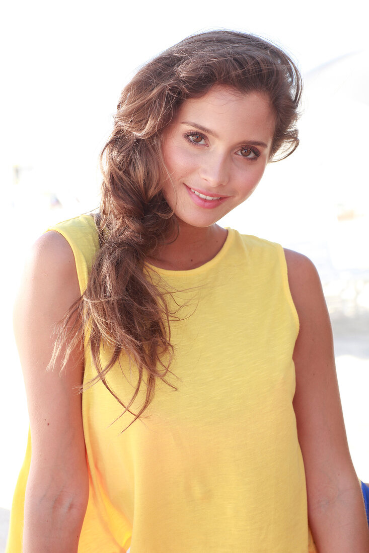 Woman with long dark hair in a yellow shirt on the beach