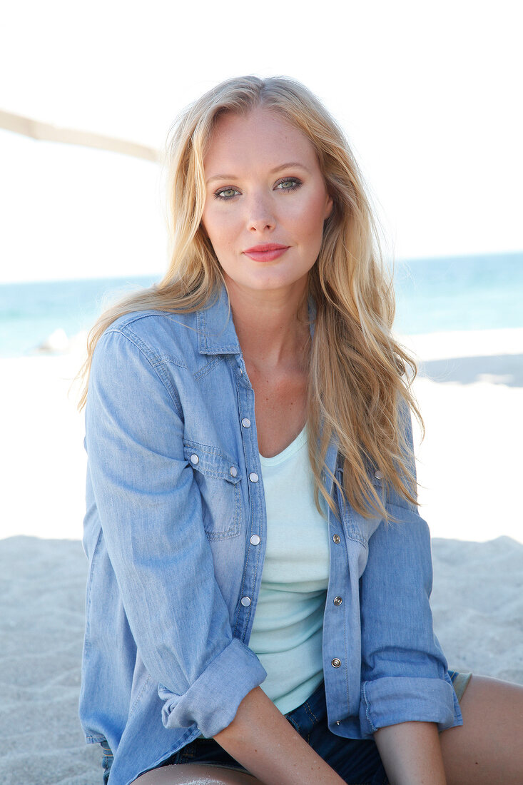 Blonde woman in a denim shirt smiles at the camera on the beach