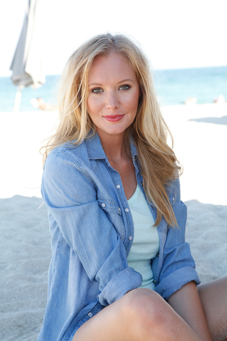 Blonde Frau im Jeanshemd lächelt in die Kamera, am Strand