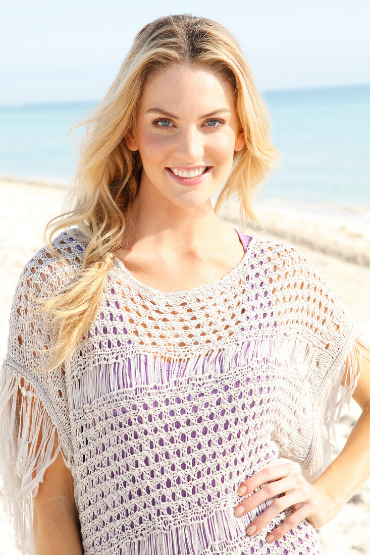 Blonde Frau mit langen Haaren in Häkelshirt am Strand