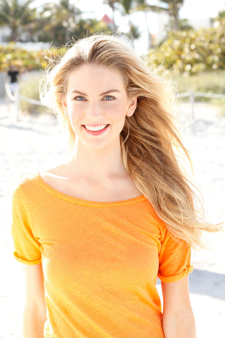 Blonde Frau mit langen Haaren in orangefarbenem T-Shirt am Strand